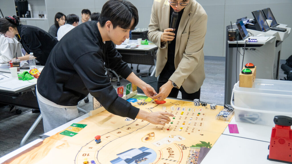 레이스 우승 낙타에 베팅하기 위해 팀을 대표하여 게임판에 칩을 올리며 마지막 승부수를 던지는 참가자와 진행을 돕는 디렉터