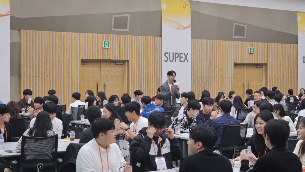 기업 팀빌딩 워크샵 현장에서 테이블 사이를 걸으며 신입사원들과 가까이 소통하고 분위기를 이끄는 팀빌딩 강사 김대현