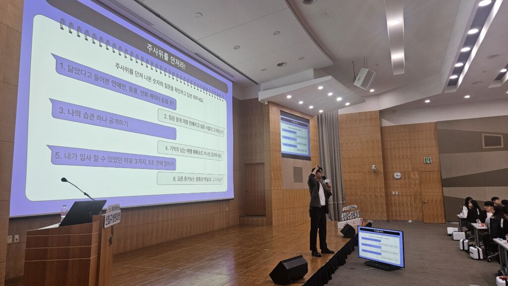 대형 스크린에 띄워진 주사위 Q&A 아이스브레이킹 프로그램의 규칙을 설명하고 있는 메모리 이벤트 팀빌딩 전문가