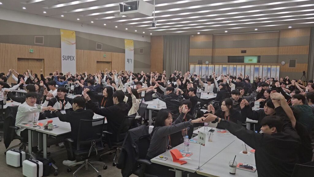 SK하이닉스 신입사원 팀빌딩 중 조원들과 손을 맞잡고 팔을 들어 올리며 환호하는 역동적인 조직활성화 프로그램 현장