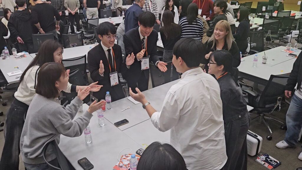 팀원들이 둥글게 모여 서서 규칙 박수 릴레이 미션을 성공하기 위해 서로 눈을 맞추며 단합하는 SK하이닉스 신입사원들