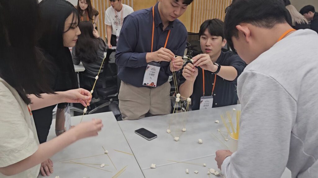 공동 목표 달성과 역할 분담을 배우기 위해 스파게티 면과 마시멜로우로 탑을 쌓으며 활발히 논의하는 팀빌딩 프로그램